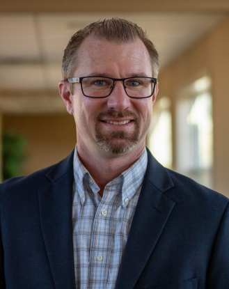 Man wearing glasses and blazer smiling indoors