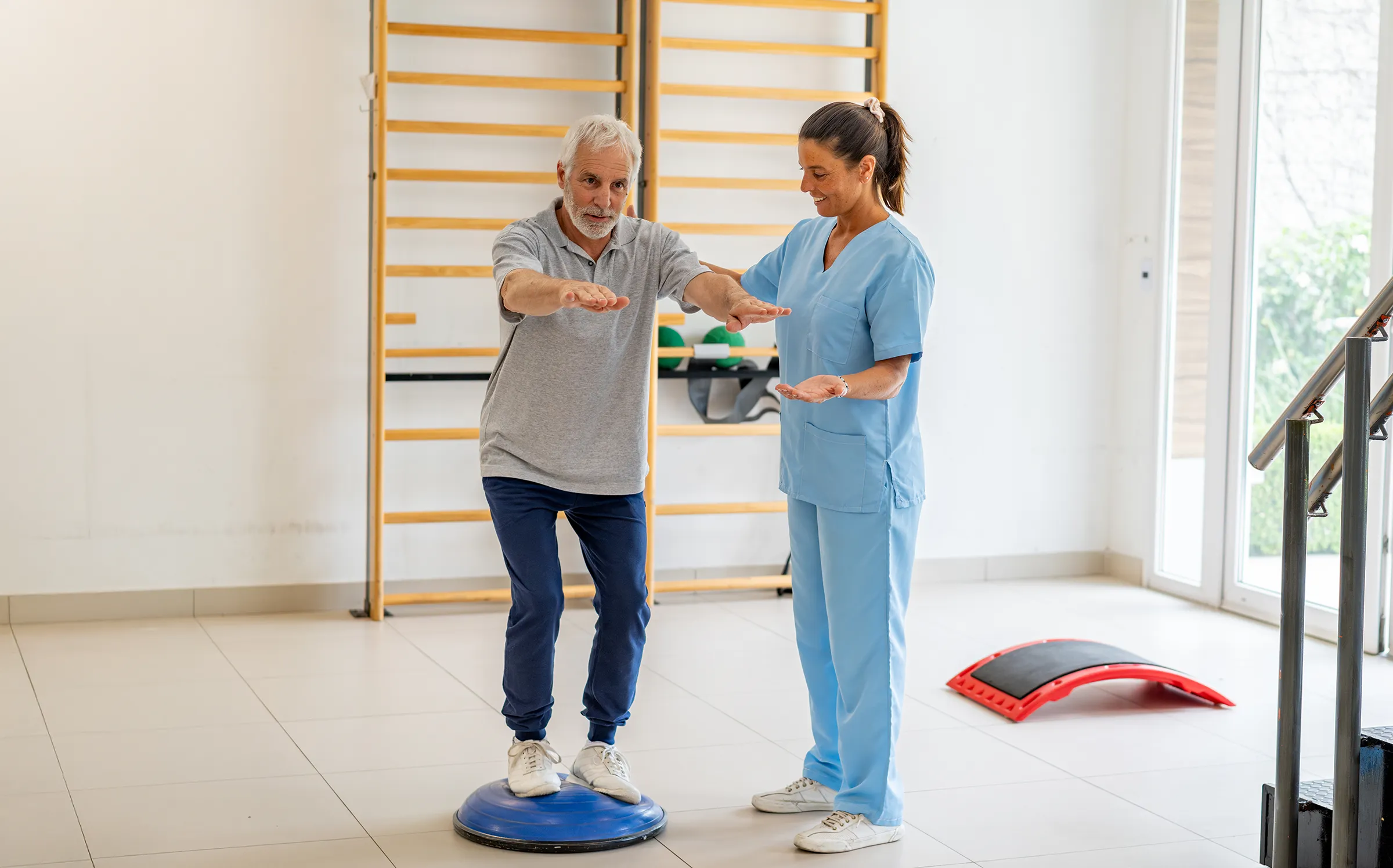 Physical therapist assists senior man with balance exercise.