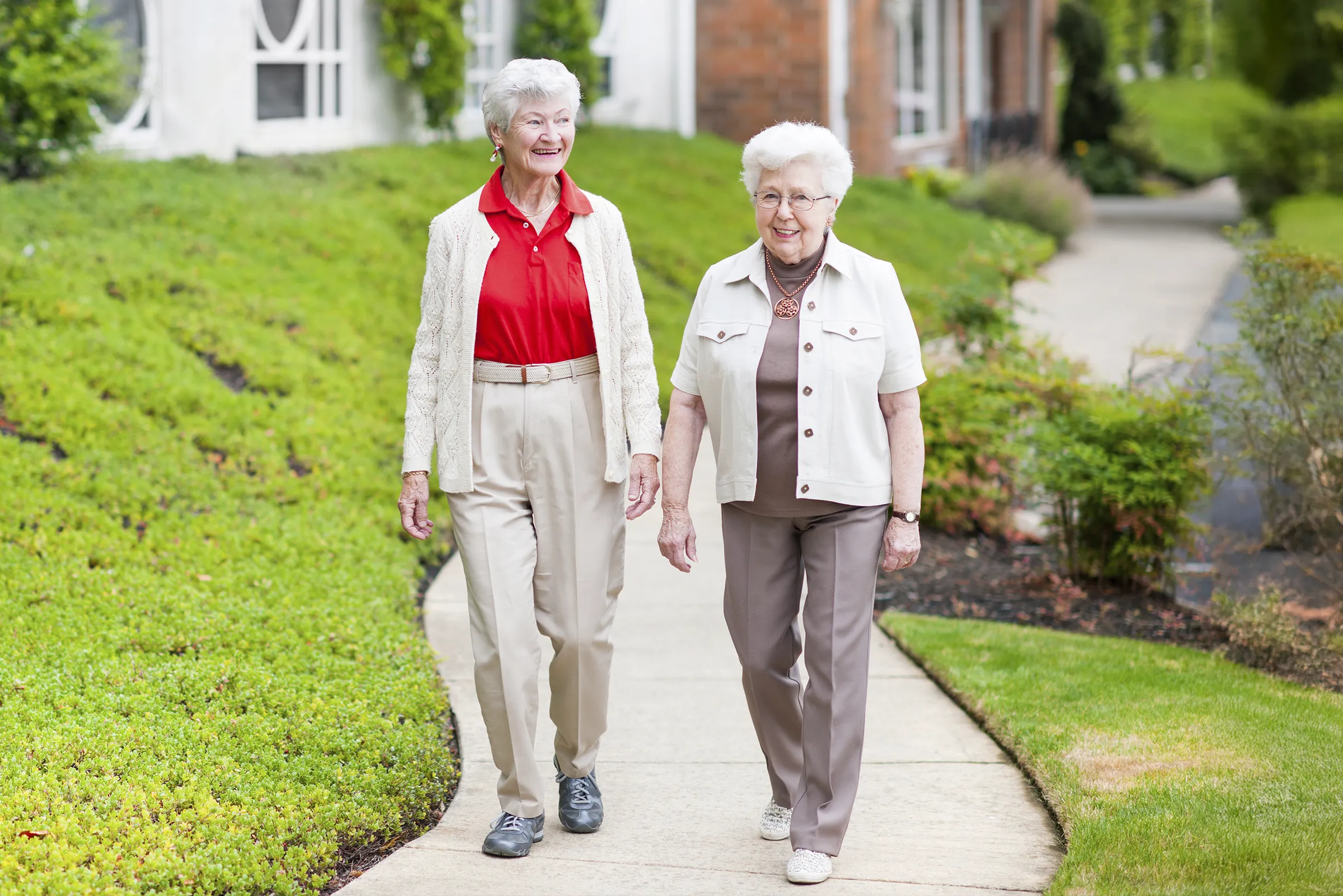 Two elderly women walking on leafy sidewalk